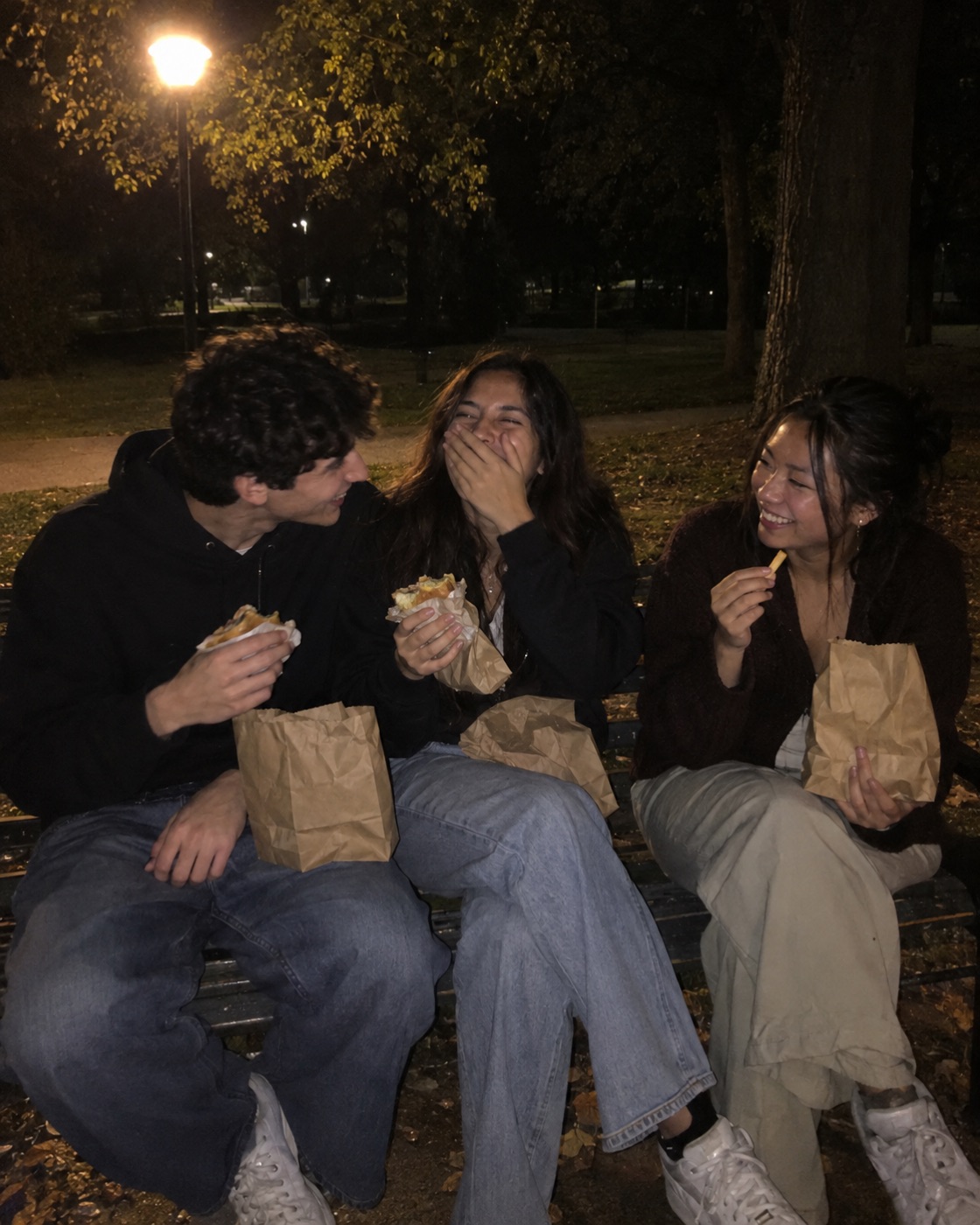 Three friends laughing on a park bench at night